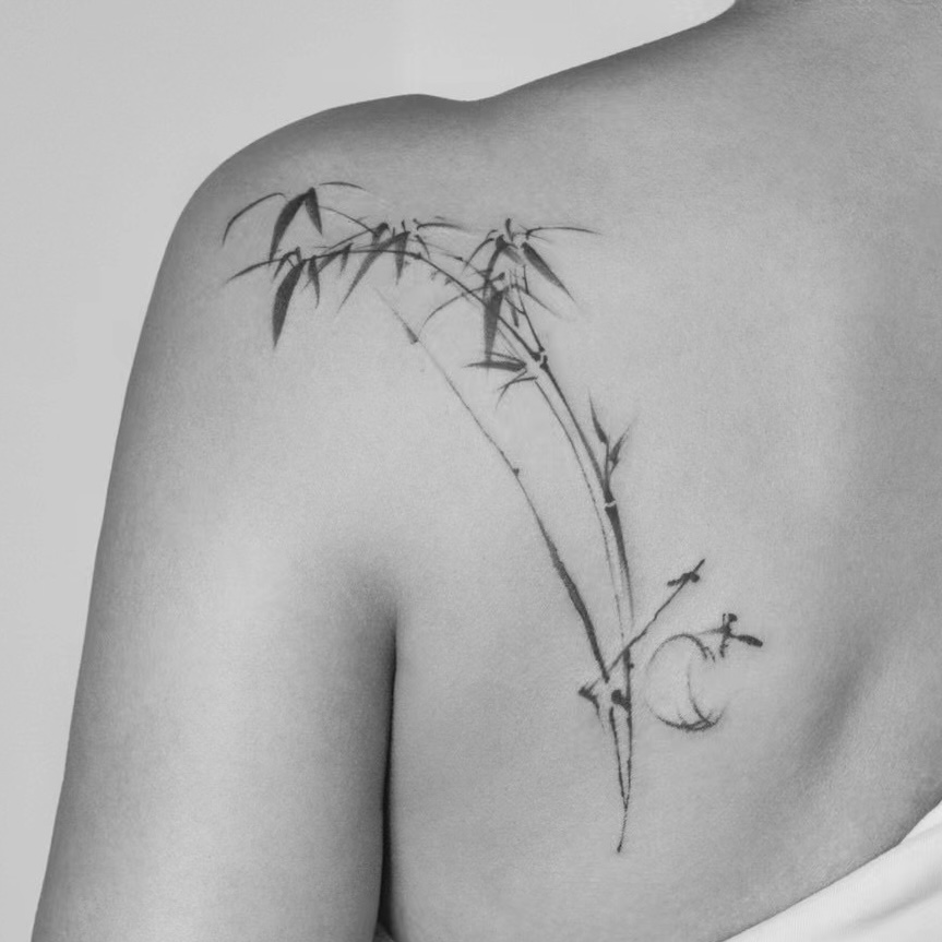 Ink-brush-style bamboo and moon tattoo across the shoulder blade